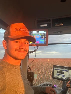 Foto do João Vitor sorridente em cabine de trator com monitores ao fundo, na agricultura de sua família, refletindo inovação no campo