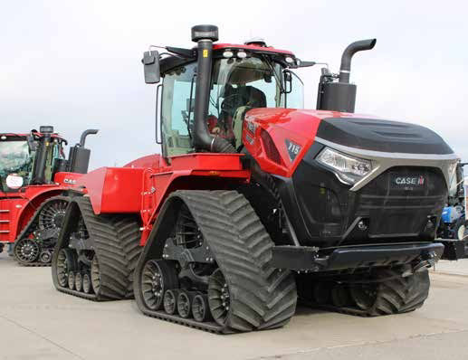 Case IH Quadtrac tractor on cement ground at a tradeshow for display. The tractor is red and black and a person in the cab. Multiple wheels form the rubber tracks on the tractor.