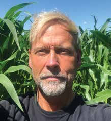 A headshot of Jason Voogt, Certified Crop Advisor for Field2Field Agronomy. They are wearing a black shirt with tall corn plants behind them. 