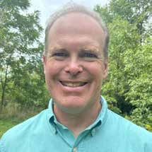 A headshot of John Greig, Senior Technology Editor for Glacier Farmmedia. They are a smiling Caucasian person with a light blue polo shirt. 