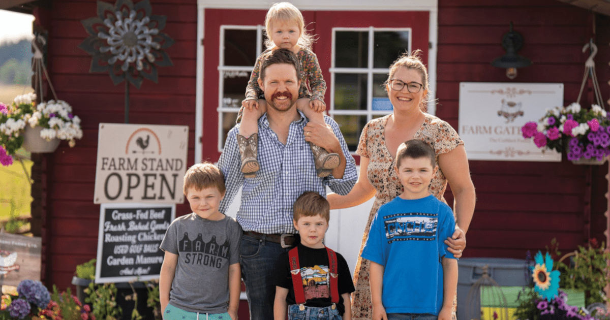 Cuthbert family standing in front of a rustic red farm shop with flowerpots and signs, promoting a local farm business and fresh produce.