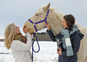 Mother and adult daughter standing with and petting a white horse