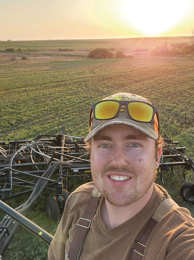 Brady Ferris standing on a large piece of machinery, taking a selfie while in the canola field. He is wearing a baseball hat. 