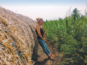 A person leaning against a bale of hay in a farm field