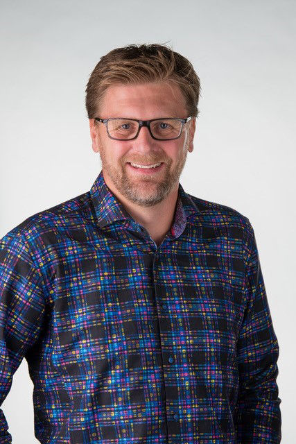 A portrait of Dan Owen, a man wearing a blue checkered shirt and dark glasses. He is smiling into the camera.