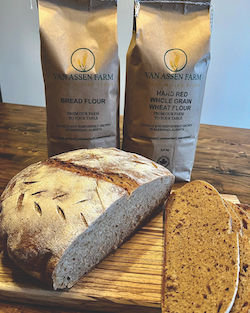 Sliced cob of bread on a cutting board, with two bags of Van Essen Farm flour