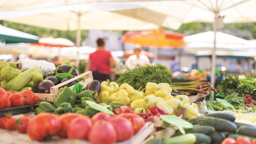 Farmers' food market stall with variety of organic vegetable. Vendor serving and chating with customers.