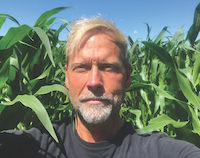 A photo of Jason Voogt, Agronomist, and owner of Field2Field Agronomy. He is standing among tall corn plants.