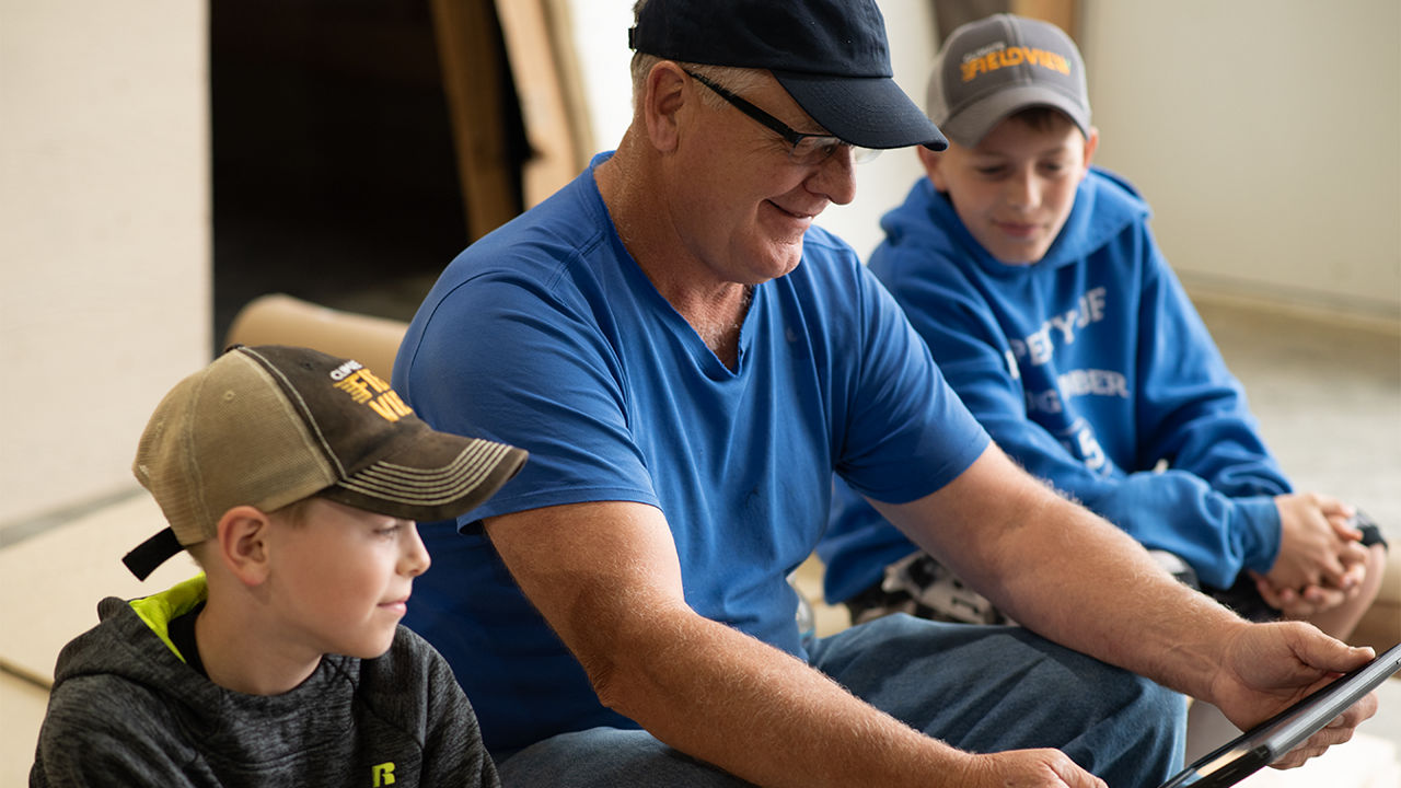 Man and two children looking at a tablet, all wearing hats