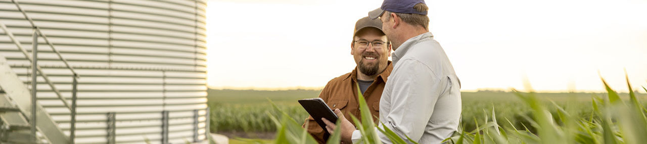Two farmers holding a tablet and smiling at each other on a green field