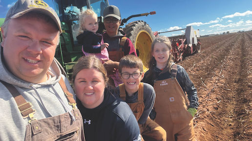 Selfie style family photo standing in a harvested crop field up against a tractor hauling farming equipment 