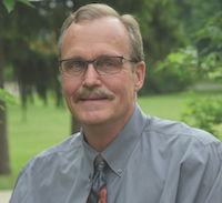 A portrait of Peter Sikkema, Professor of Field Crop Weed Management at the University of Guelph. He is wearing a grey button up short and a colourful tie.