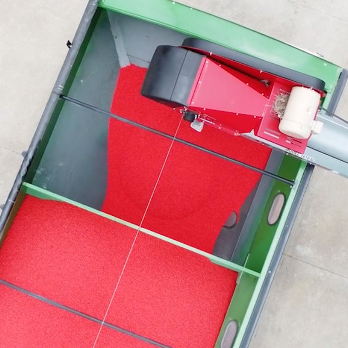 Top view of bright red treated seeds inside agricultural planting equipment. 