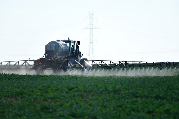 A blue tractor sprays a green field