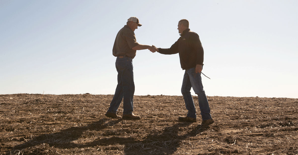 Two farmers shaking hands in empty field 